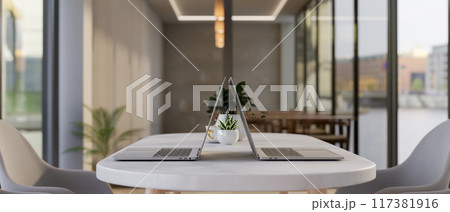 Two laptop computers on a modern white table in a contemporary meeting room or co-working space. 117381916