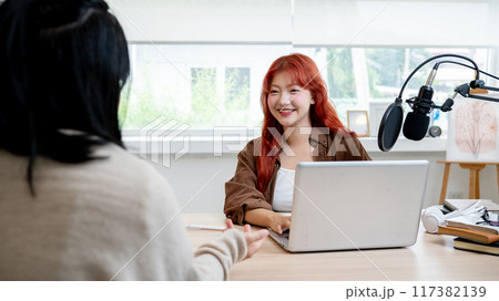 A beautiful and friendly Asian female radio host or podcaster is interviewing a guest in her studio. A beautiful and friendly Asian female radio host or podcaster is interviewing a guest in her studio. 117382139
