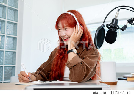 A charming Asian female radio host is conducting a remote interview from her studio. A charming Asian female radio host is conducting a remote interview from her studio. 117382150