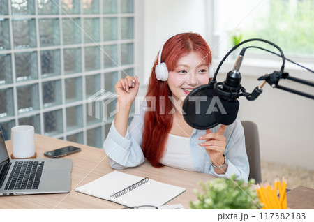 A beautiful Asian female podcaster is recording her podcast in the studio, speaking into a mic. A beautiful Asian female podcaster is recording her podcast in the studio, speaking into a mic. 117382183