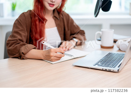 A beautiful Asian female podcaster is focusing on adjusting the script for the new podcast episode. 117382236