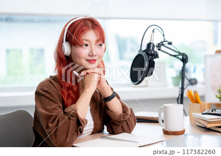 A thoughtful Asian female podcaster is listening to her guest during a remote interview. 117382260