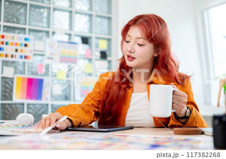 A graphic designer is selecting colors from a set of color swatches while having a morning coffee. 117382268