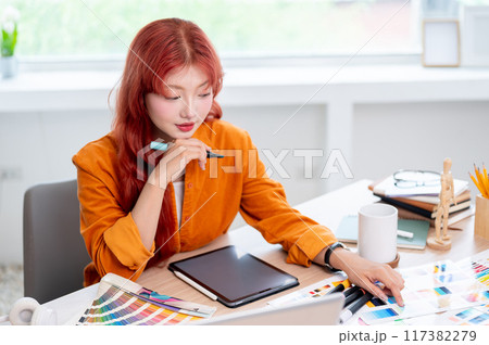 A creative, focused Asian female graphic designer is working at her desk in the studio. A creative, focused Asian female graphic designer is working at her desk in the studio. 117382279