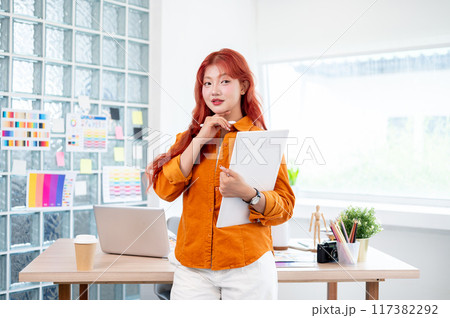 A confident female graphic designer stands in her studio with a graphic drawing tablet in her hand. A confident female graphic designer stands in her studio with a graphic drawing tablet in her hand. 117382292