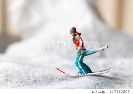 Miniature figurine of a skier in motion skiing across a white snowy landscape 117383207