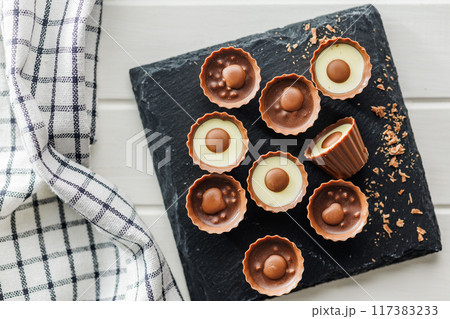 Sweet pralines. Chocolate truffles on cutting board on white table. Top view. Sweet pralines. Chocolate truffles on cutting board on white table. Top view. 117383233