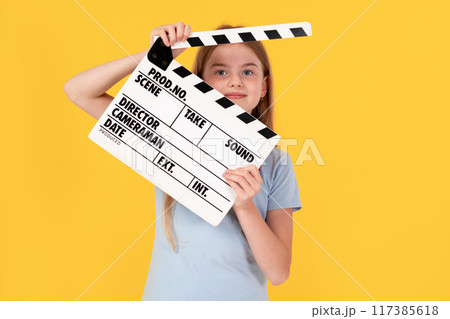 Little child girl wear blue t-shirt holding clapperboard isolated on yellow background. Children lifestyle childhood concept. Little child girl wear blue t-shirt holding clapperboard isolated on yellow background. Children lifestyle childhood concept. 117385618