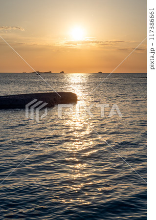 Vertical photo of Cala Conta beach sunset, low sun casting reflections on dark, textured sea surface 117386661
