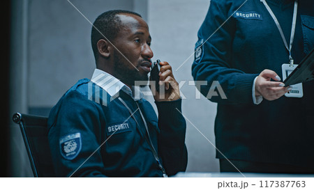 African American security officer talks in walkie talkie. Female coworker uses tablet African American security officer talks in walkie talkie. Female coworker uses tablet 117387763