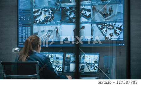 Female CCTV operator works on computer with security cameras, talks on walkie talkie Female CCTV operator works on computer with security cameras, talks on walkie talkie 117387785