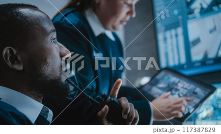 Female worker talks with security officer, uses tablet with surveillance footage Female worker talks with security officer, uses tablet with surveillance footage 117387829