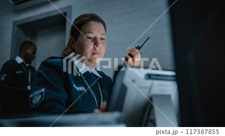 Female security officer or dispatch talks in walkie talkie in monitoring center Female security officer or dispatch talks in walkie talkie in monitoring center 117387855