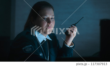 Female security officer uses walkie talkie sitting at workplace in monitoring center Female security officer uses walkie talkie sitting at workplace in monitoring center 117387913