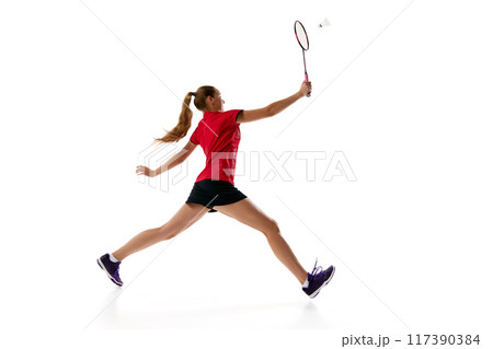 Side view photo of young woman in uniform with rocket, badminton player leaping to hits shuttlecock against white studio background. Side view photo of young woman in uniform with rocket, badminton player leaping to hits shuttlecock against white studio background. 117390384