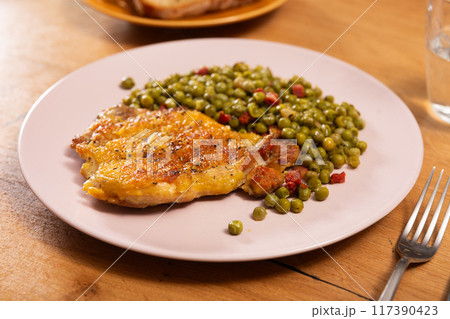 Fried boneless skinless chicken leg with green peas for garnish on plate 117390423