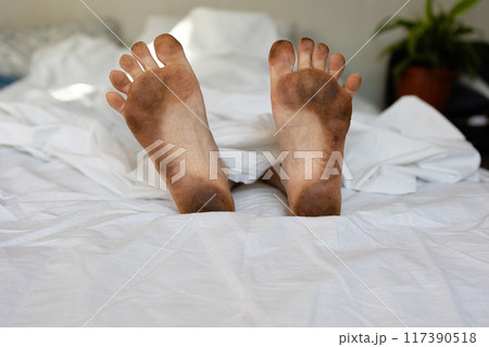 Dirty feet are sticking out from under the blankets on a bed Dirty feet are sticking out from under the blankets on a bed 117390518