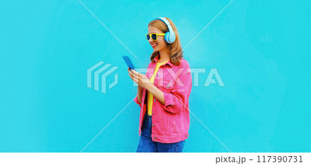 Portrait of stylish modern happy smiling young woman in headphones listening to music with phone Portrait of stylish modern happy smiling young woman in headphones listening to music with phone 117390731