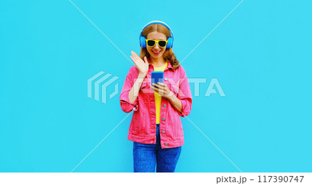 Portrait of stylish modern happy smiling young woman in headphones listening to music with phone Portrait of stylish modern happy smiling young woman in headphones listening to music with phone 117390747