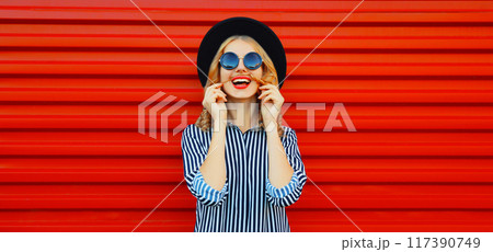Portrait of funny cheerful laughing young woman showing mustache her hair on red background Portrait of funny cheerful laughing young woman showing mustache her hair on red background 117390749