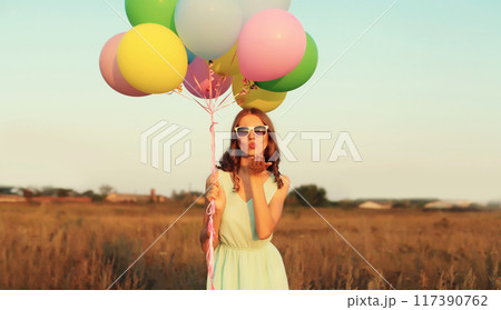 Cute young woman with bunch of colorful balloons outdoors in field Cute young woman with bunch of colorful balloons outdoors in field 117390762