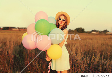 Happy cute smiling young woman with bunch of colorful balloons wearing dress outdoors Happy cute smiling young woman with bunch of colorful balloons wearing dress outdoors 117390763