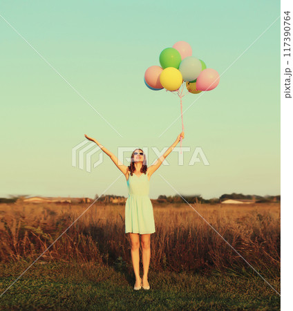 Happy cute smiling young woman with bunch of colorful balloons wearing dress outdoors Happy cute smiling young woman with bunch of colorful balloons wearing dress outdoors 117390764
