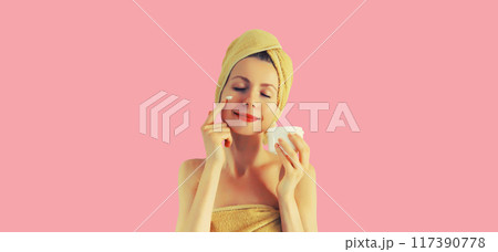 Portrait happy smiling young woman applying face cream drying hair in bath towel on pink background Portrait happy smiling young woman applying face cream drying hair in bath towel on pink background 117390778