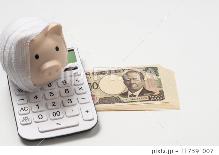 包帯に巻かれた貯金箱と新紙幣と電卓で医療費のイメージ 117391007