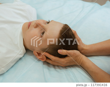 Osteopathy Treatment. Boy's head being manipulated by real osteopathic physician. Naturopath treats kid with osteopathy as alternative medicine and therapy. Osteopath harmonizes body 117391416