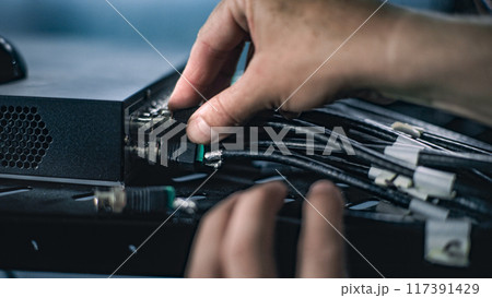 Close up of male network administrator inserting cables into server rack 117391429