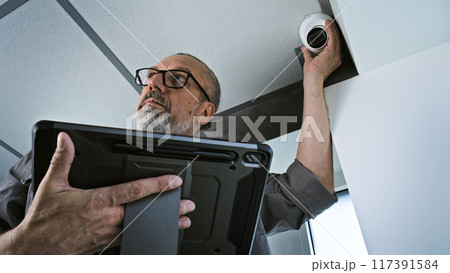 Male installer adjusts the angle of CCTV camera in office, uses tablet computer Male installer adjusts the angle of CCTV camera in office, uses tablet computer 117391584