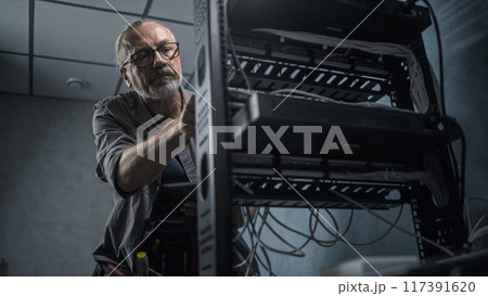 Male network administrator works in server room using tablet computer Male network administrator works in server room using tablet computer 117391620