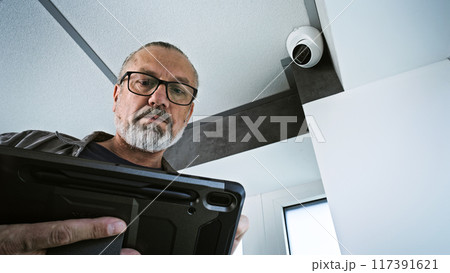 Male installer adjusts the angle of CCTV camera in office, uses tablet computer 117391621