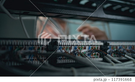 Male system administrator connects cables with server rack Male system administrator connects cables with server rack 117391668
