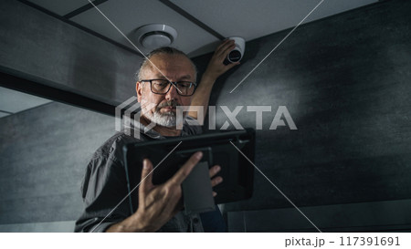 Male installer uses tablet computer to set up surveillance camera in office space 117391691