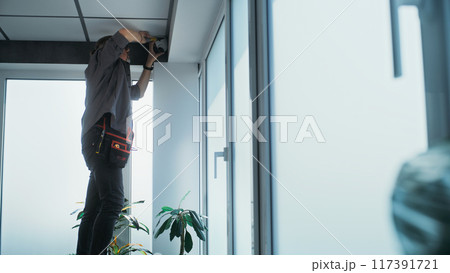 Male technician screws security camera to the ceiling in office Male technician screws security camera to the ceiling in office 117391721