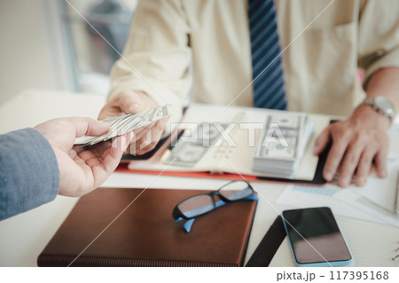 Man offering batch of hundred dollar bills. Hand of a businessman giving money to his partner. Hand receiving money from businessman. Venality, bribe, corruption concept. 117395168