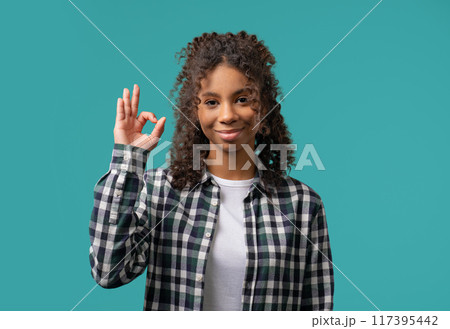 Positive teenager girl with hand sign Ok, Okay gesture.Lady on blue studio 117395442