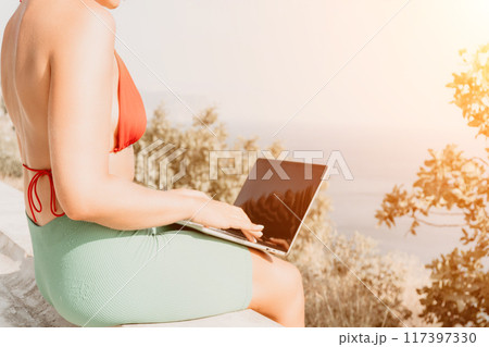Woman laptop park. Working remotely on seashore. Happy successful woman female freelancer working on laptop at summer sunset, makes a business transaction online. Freelance, remote work on vacation 117397330