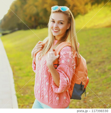 Portrait of happy smiling young blonde woman with backpack outdoors in the park Portrait of happy smiling young blonde woman with backpack outdoors in the park 117398330