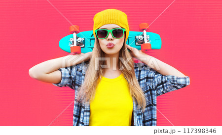 Portrait stylish cool woman with skateboard wearing colorful yellow hat on pink background 117398346