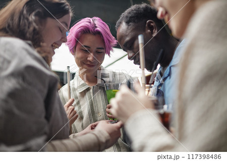 Group of young adults enjoying time together at a modern gathering event while chatting and using gadgets. Multiracial friends forming close connections Group of young adults enjoying time together at a modern gathering event while chatting and using gadgets. Multiracial friends forming close connections 117398486