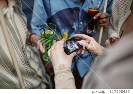 Group of people socializing, holding drinks while someone is taking a picture with a compact digital camera during gathering 117398487