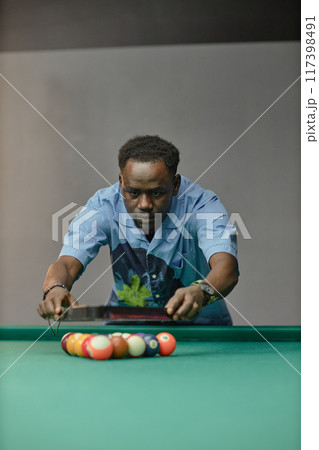 Man aligning billiard balls on table, concentrating on placement Proper focus and skill required for perfect game shot Billiards player deeply immersed in task 117398491