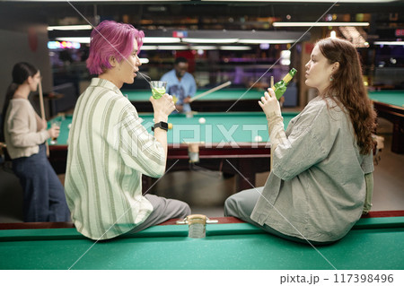 Group of friends enjoying conversation and drinks while playing billiards at a dimly lit lounge. People engaging in leisure activity and bonding over a shared hobby Group of friends enjoying conversation and drinks while playing billiards at a dimly lit lounge. People engaging in leisure activity and bonding over a shared hobby 117398496