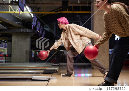 Two friends engaging in bowling game in modern indoor alley with one preparing to throw ball while other observes in background 117398522