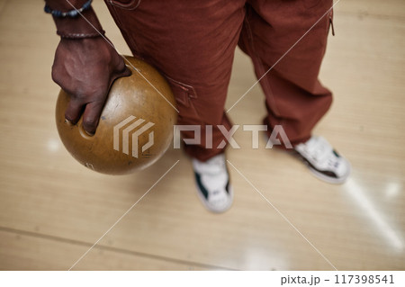 Hand holding a bowling ball, preparing for a shot at bowling alley. Earth-toned pants and casual shoes are visible, capturing focus on the hand's grip on ball Hand holding a bowling ball, preparing for a shot at bowling alley. Earth-toned pants and casual shoes are visible, capturing focus on the hand's grip on ball 117398541