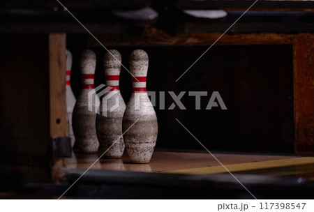 Close-up shot of four worn bowling pins standing in row within dimly lit bowling alley lane with reflections on floor creating atmospheric effect 117398547