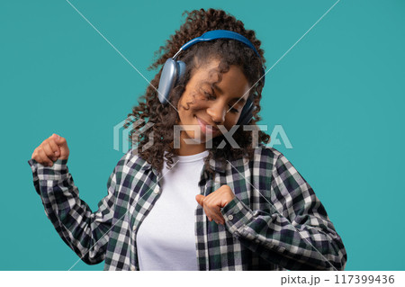 African woman listening streaming music,enjoying dance with headphones on blue African woman listening streaming music,enjoying dance with headphones on blue 117399436
